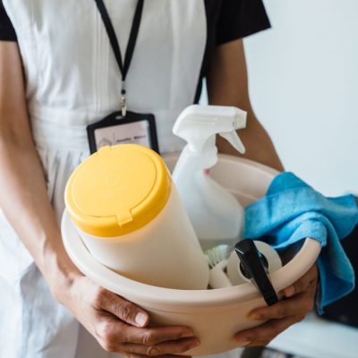 A uniformed cleaner holding a basin with cleaning supplies indoors. Ideal for cleaning and sanitation themes.